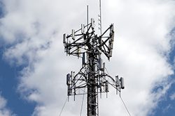 A cellular antenna tower isolated over a blue sky with white fluffy clouds.